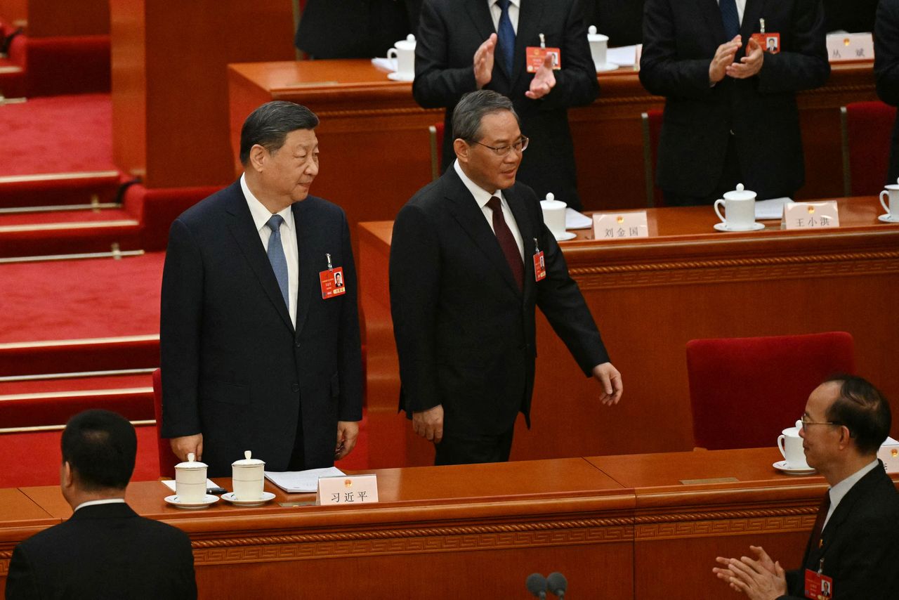 Участники сессии Всекитайского собрания народных представителей встречают аплодисментами председателя КНР Си Цзиньпина (слева) и председателя Госсовета Ли Цяна, 8 марта 2025 г., Пекин (© AFP/Jiji Press)
