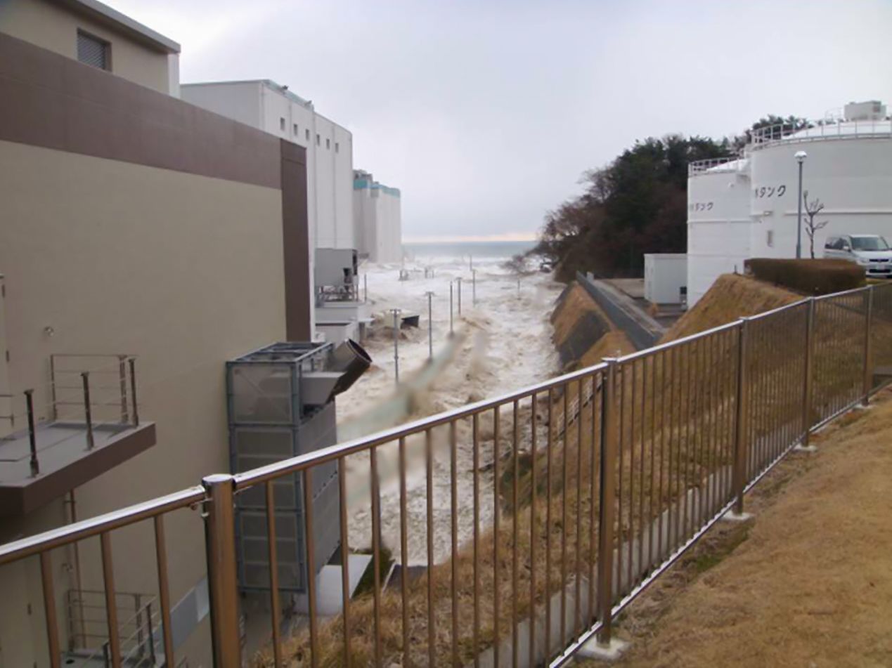 Волны цунами штурмуют склон рядом со зданиями энергоблоков (фотография предоставлена TEPCO HD / часть изображения обработана)