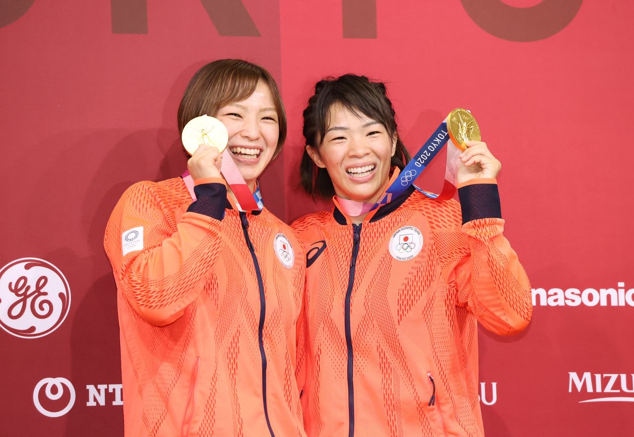 Рисако Каваи (справа) и ее младшая сестра Юкако с улыбкой демонстрируют свои золотые медали Олимпиады в женской вольной борьбе, 5 августа 2021 г., Тиба, комплекс Макухари мэссэ (© Jiji Press)