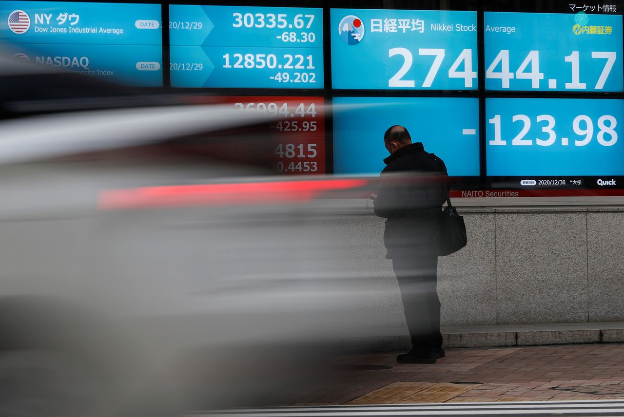 A man stands in front of a screen displaying Nikkei share average and the world