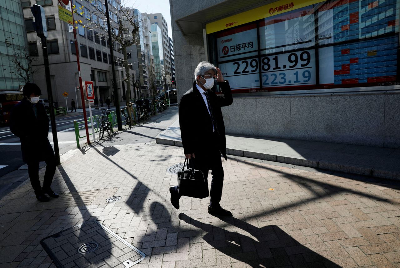 FILE PHOTO: People wearing surgical masks walk past a screen showing Nikkei index outside a brokerage in Tokyo, Japan February 3, 2020. REUTERS/Kim Kyung-Hoon/File Photo