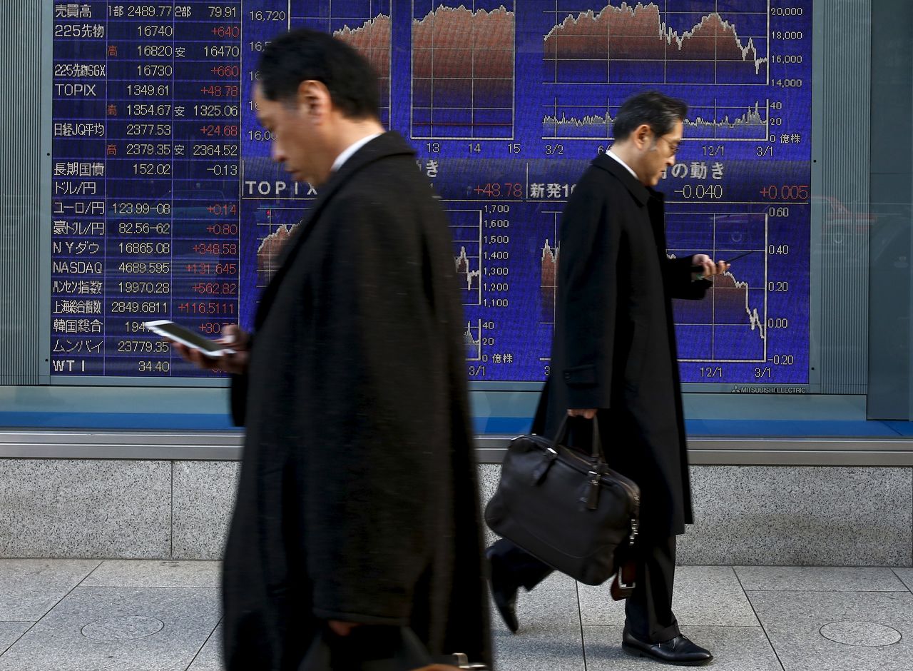 Men walk past an electronic board showing market indices outside a brokerage in Tokyo, Japan,  March 2, 2016.  Japan