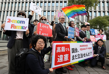 同性婚訴訟の福岡高裁判決を受け「違憲」などと書かれた横断幕やボードを掲げる原告ら=13日午前、福岡市中央区