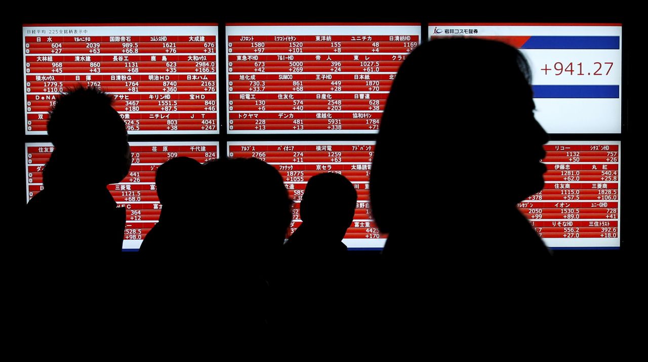 Pedestrians walk past an electronic stock quotation board outside a brokerage in Tokyo, Japan January 22, 2016. Japan