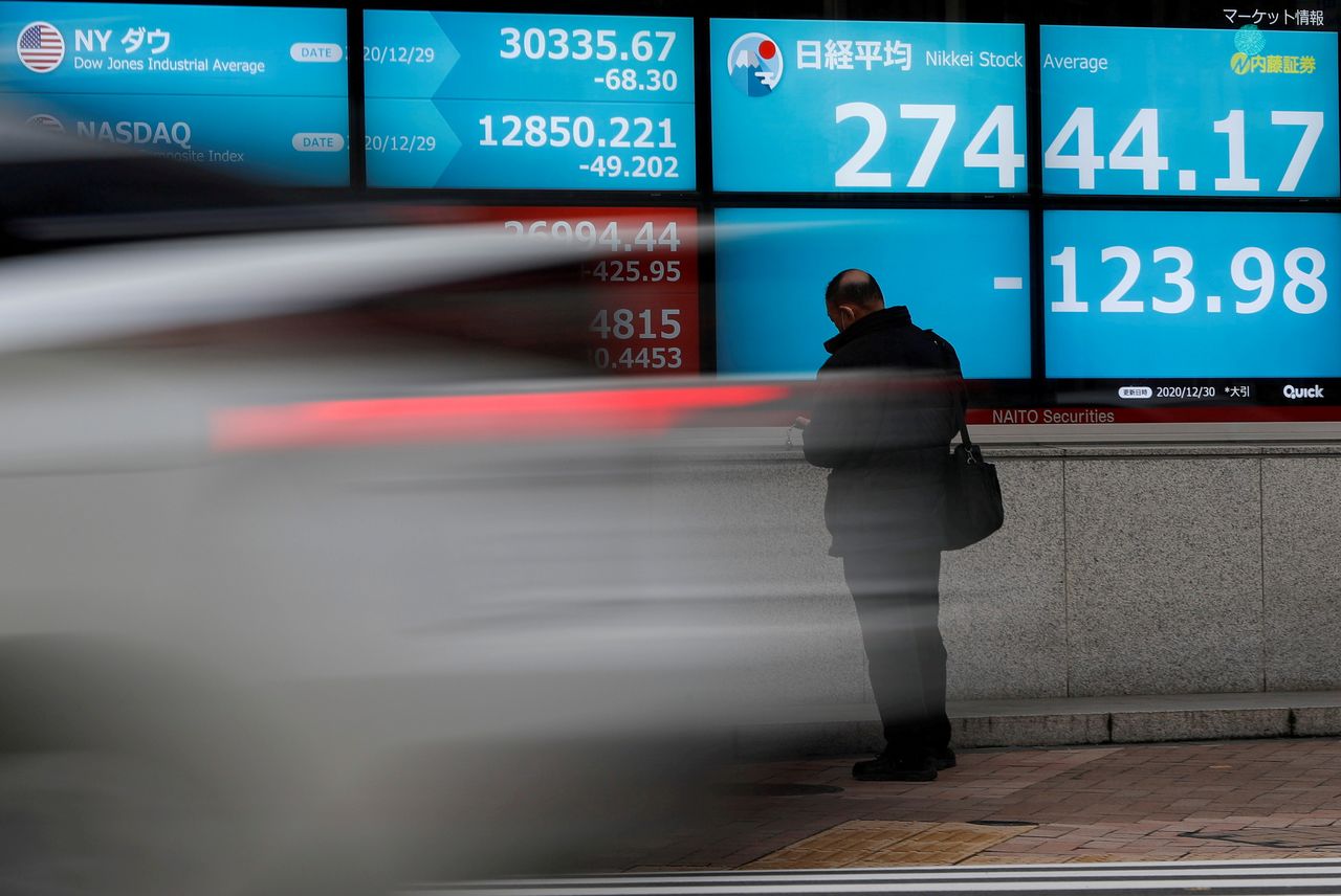 FILE PHOTO: A man stands in front of a screen displaying Nikkei share average and the world