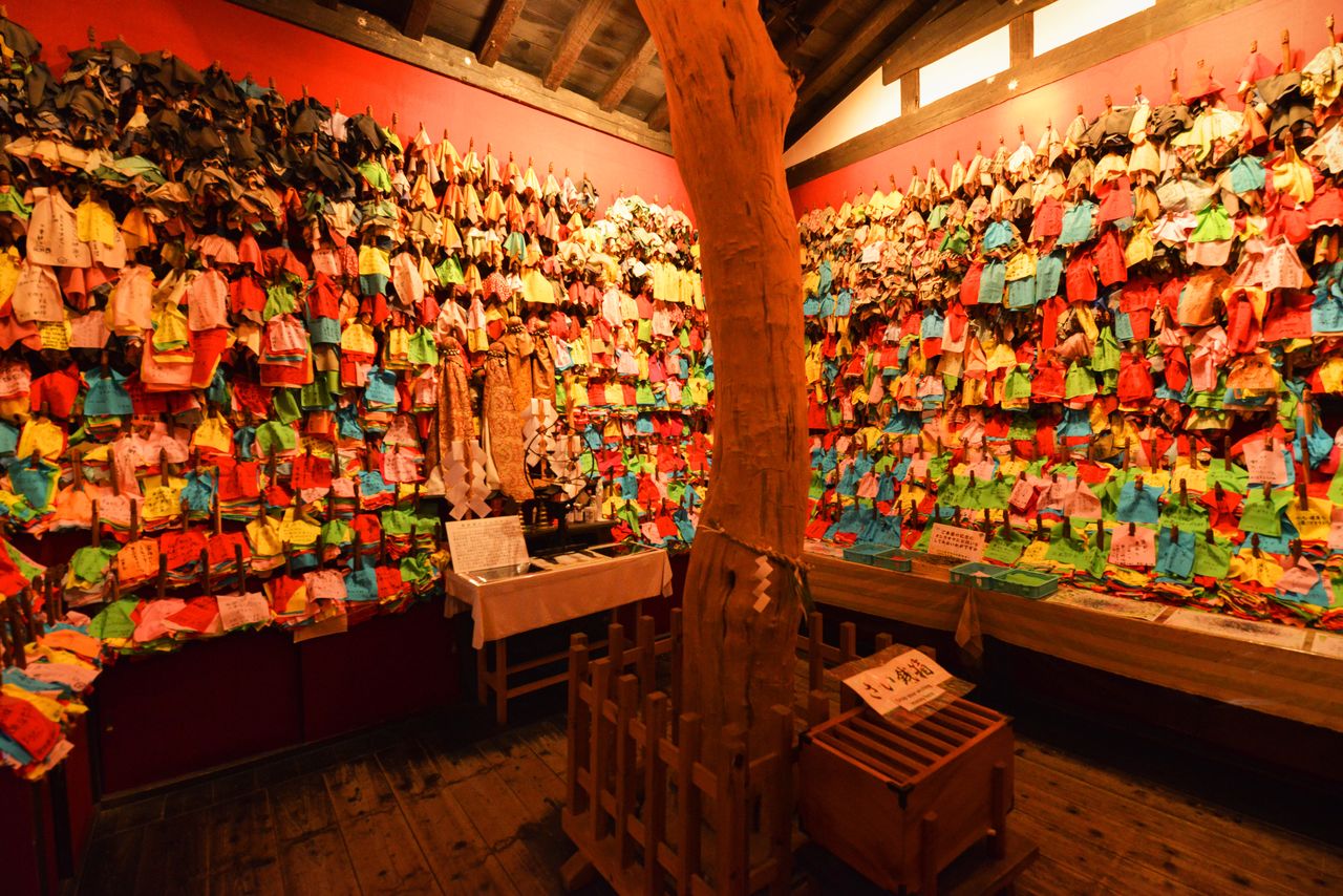 御神木を囲む赤い壁一面にオシラサマが飾られている